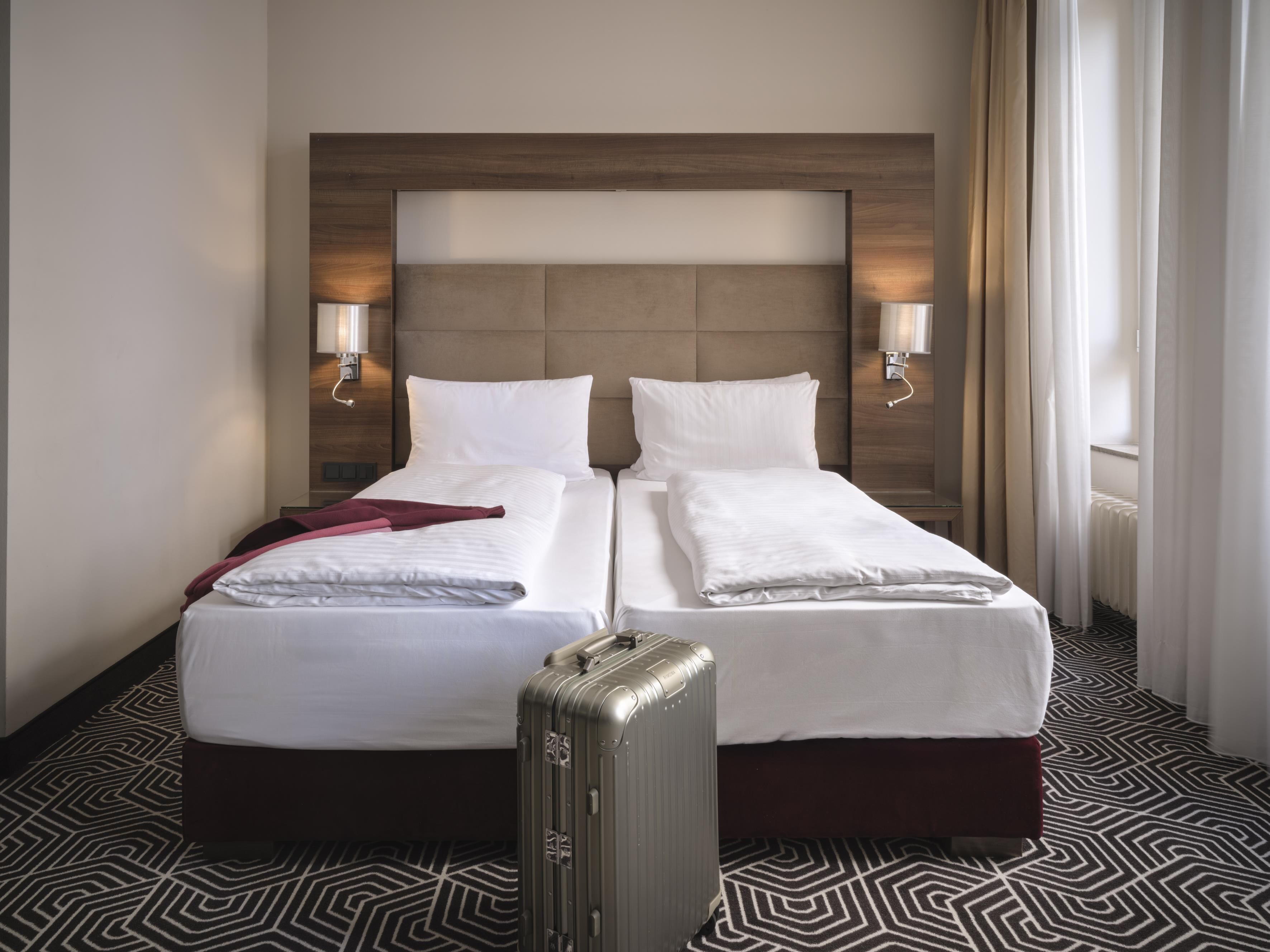 A hotel room with two beds, a wooden headboard, bedside lamps, and a patterned floor.