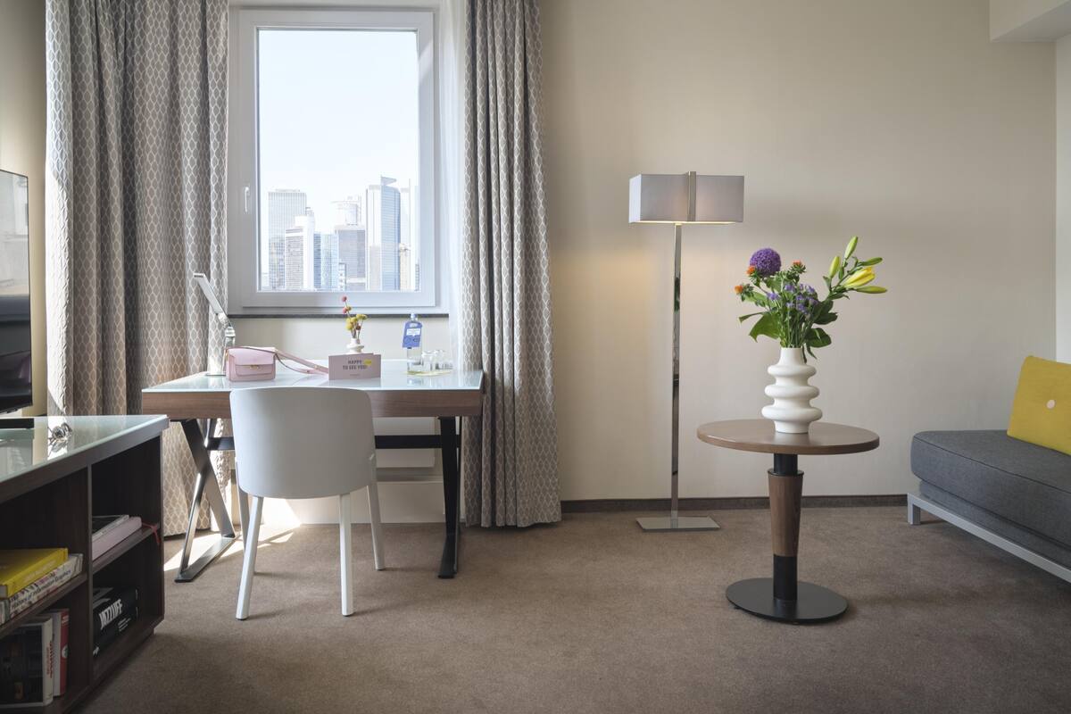 Ett hotellrum med ett skrivbord, en stol, en soffa och utsikt över stadsbilden genom fönstret.