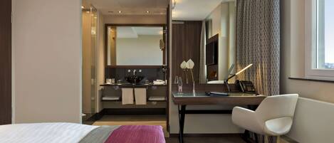 Een hotelkamer met een bed, een bureau, een stoel, een badkamer en een groot raam.