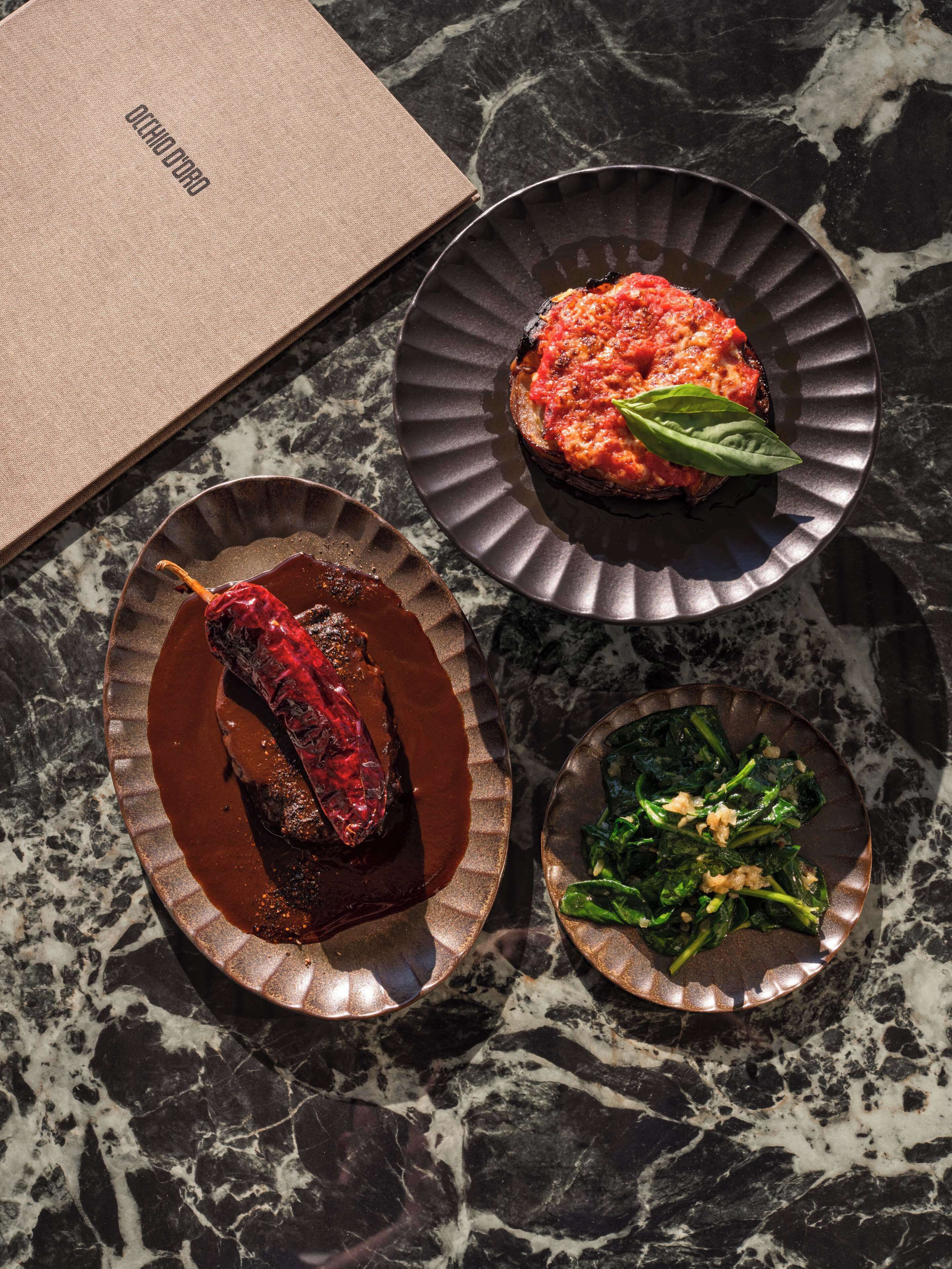 A table with three dishes: a grilled pepper, a tomato-based dish, and a spinach dish.