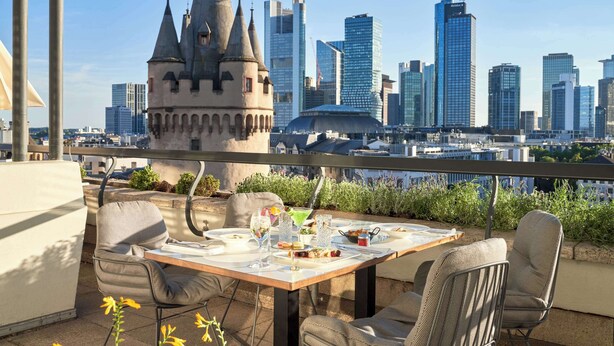A dining table with chairs on a balcony with a city skyline view.