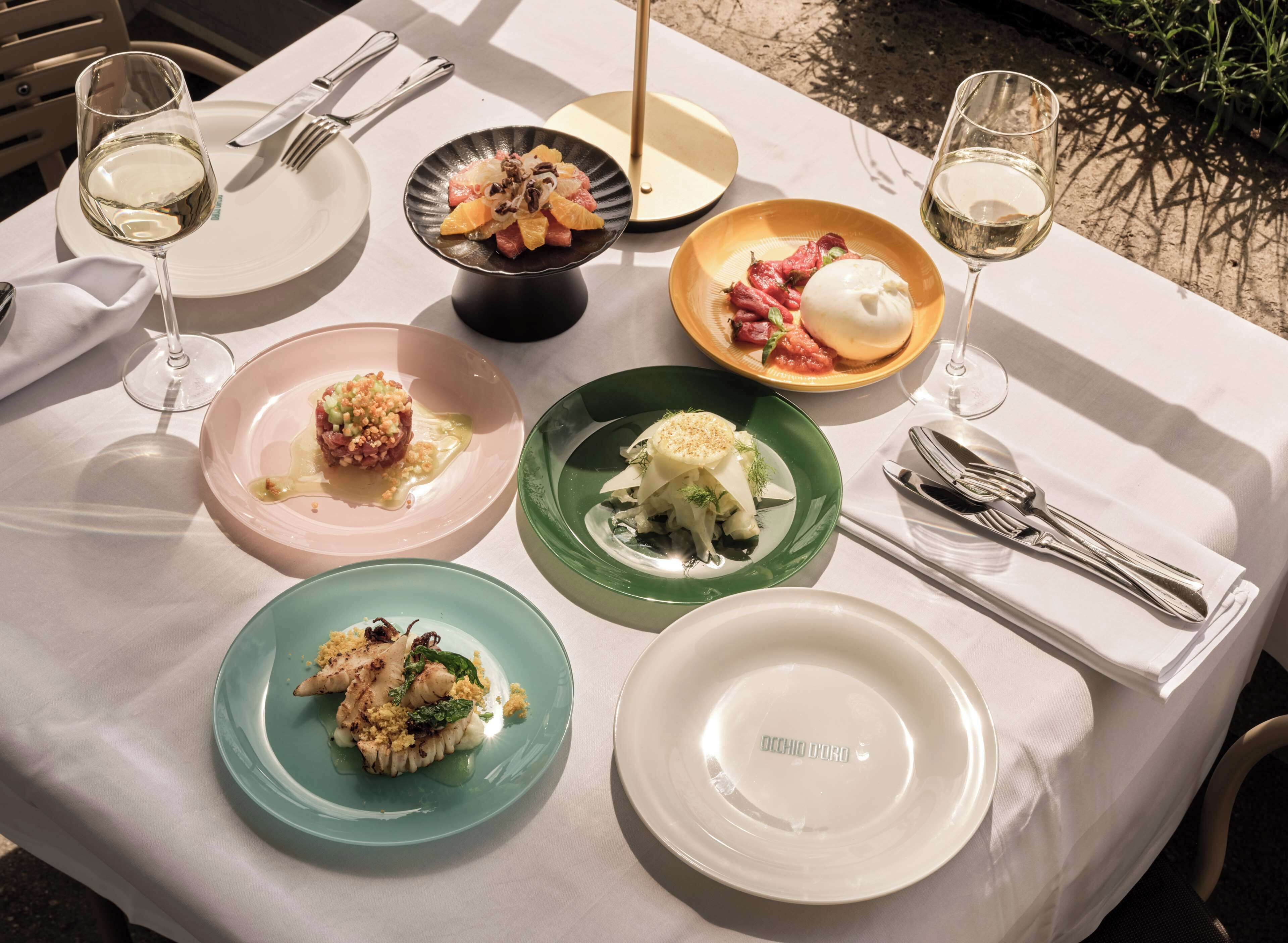 A table set for a meal with various dishes, glasses of white wine, and neatly arranged cutlery.