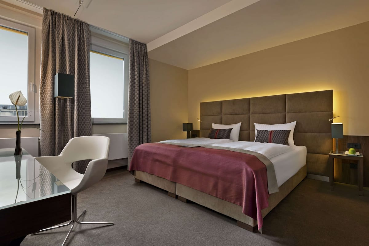 Ett hotellrum med en säng, ett skrivbord, en stol och utsikt över staden.