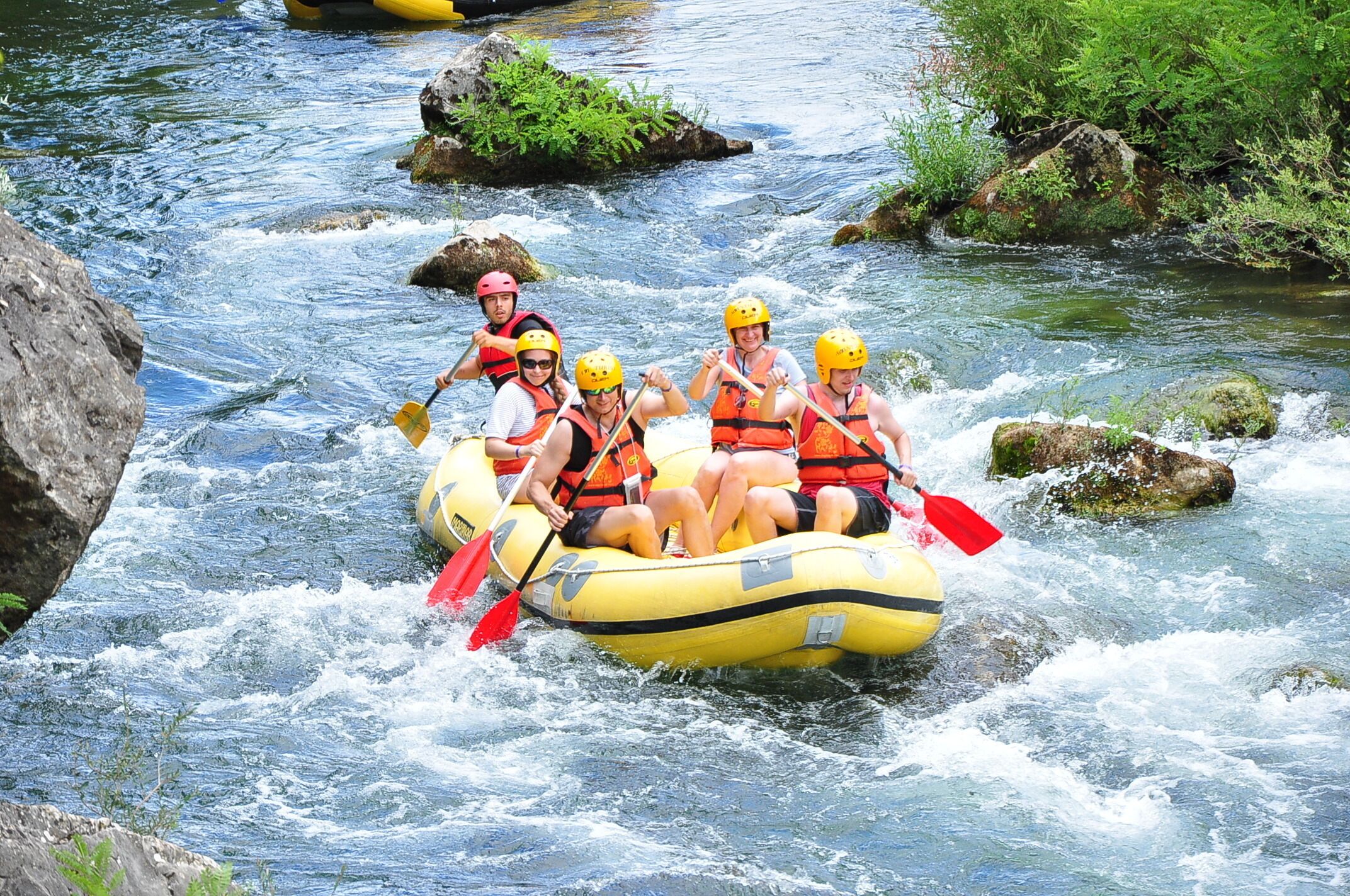 A group of people in a yellow raft navigating a river with rapids.