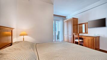 A hotel room with a bed, a desk, a chair, a TV, and a window with curtains.