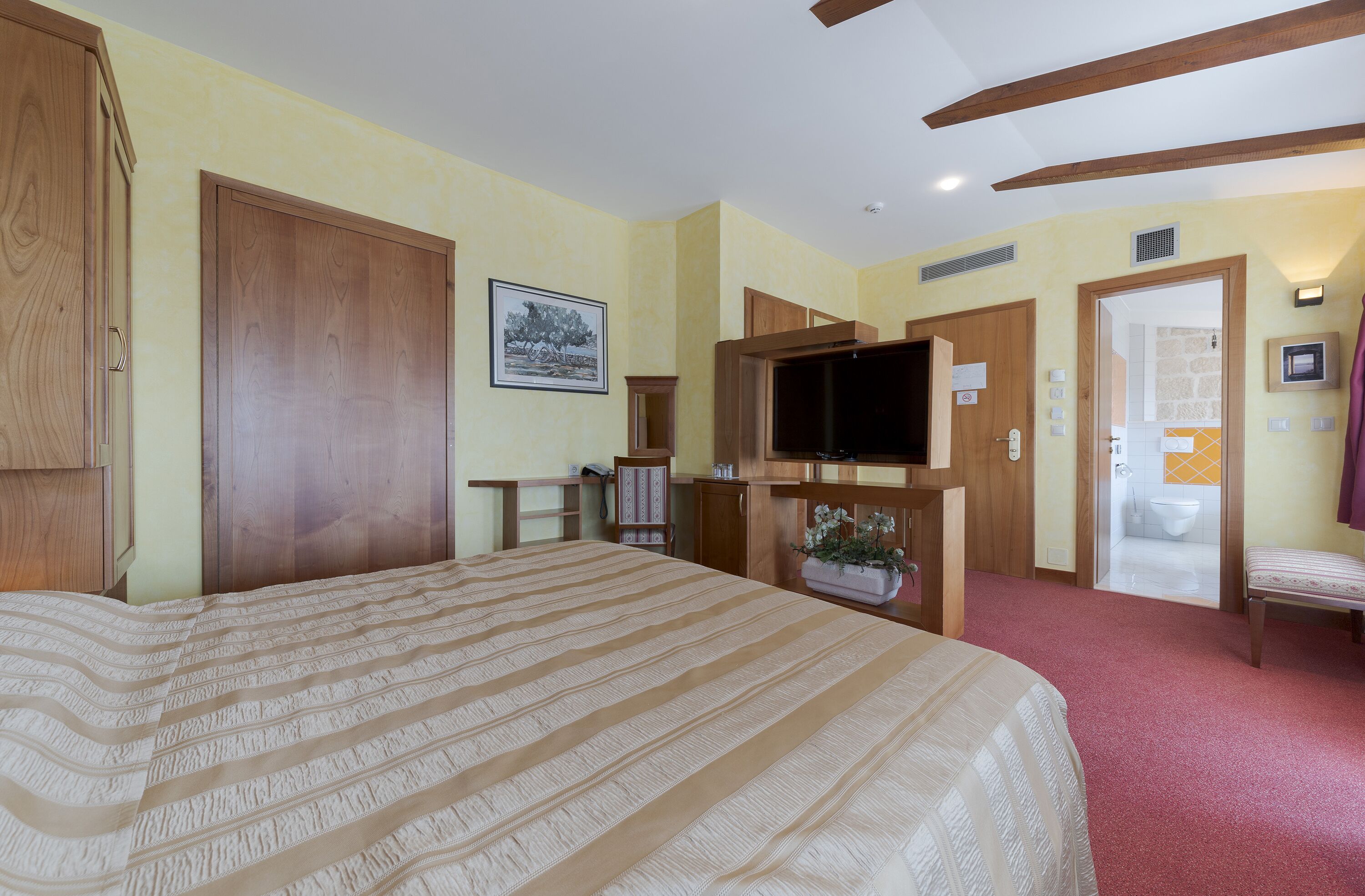 A hotel room with a large bed, wooden wardrobe, television, and a small table with a plant.