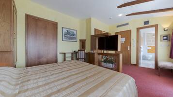 A hotel room with a large bed, wooden wardrobe, television, and a small table with a plant.