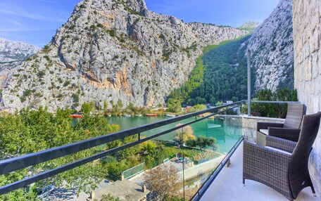 A balcony with wicker furniture overlooking a river and mountains.