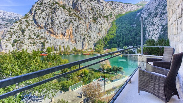 Un balcón con mobiliario de mimbre que da a un río y montañas.