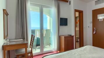 A hotel room with a bed, a desk, a chair, a television, and a sliding glass door leading to a balcony.
