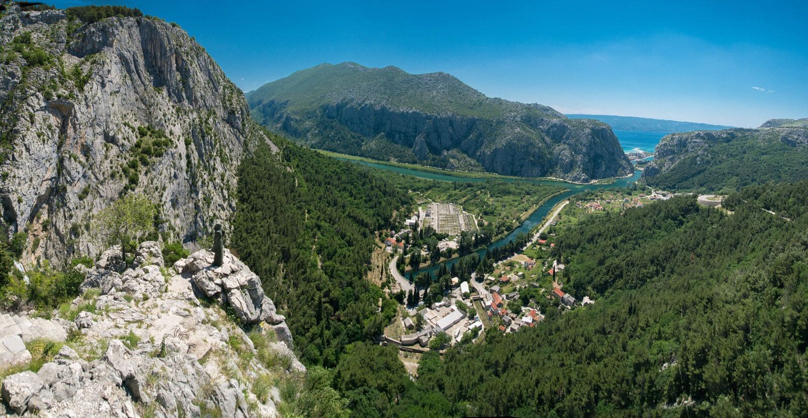 Un paisaje montañoso con un río, un pequeño asentamiento y un imponente risco.