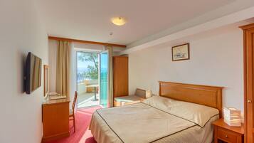 A hotel room with a bed, a desk, a chair, a TV, and a view of the outdoors.