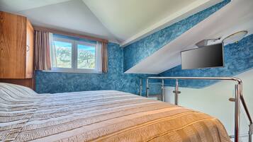 A bedroom with a bed, a window, a TV mounted on the wall, and a view of the outdoors.