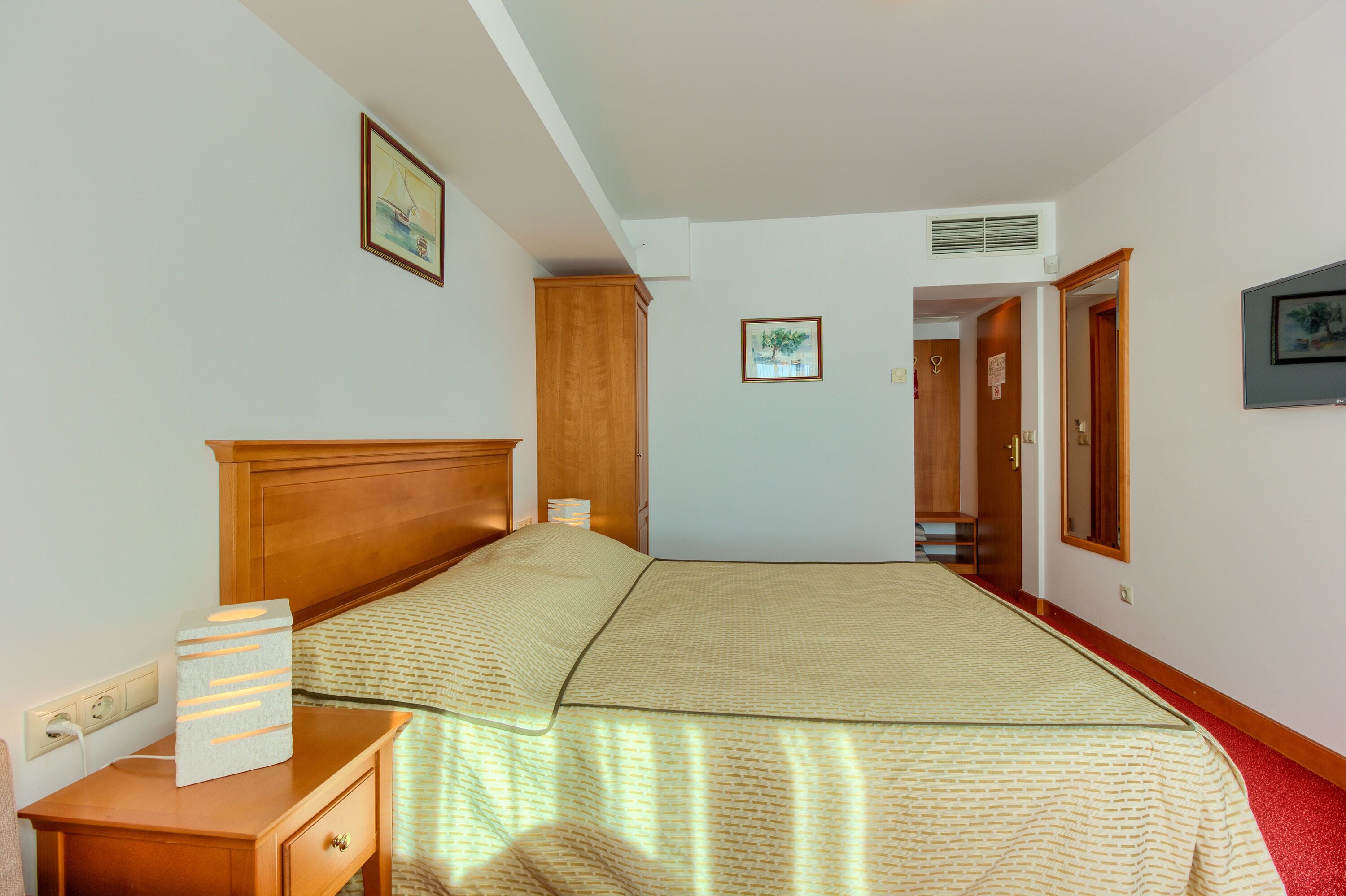A bedroom with a bed, bedside tables, a wardrobe, and a door leading to another room.
