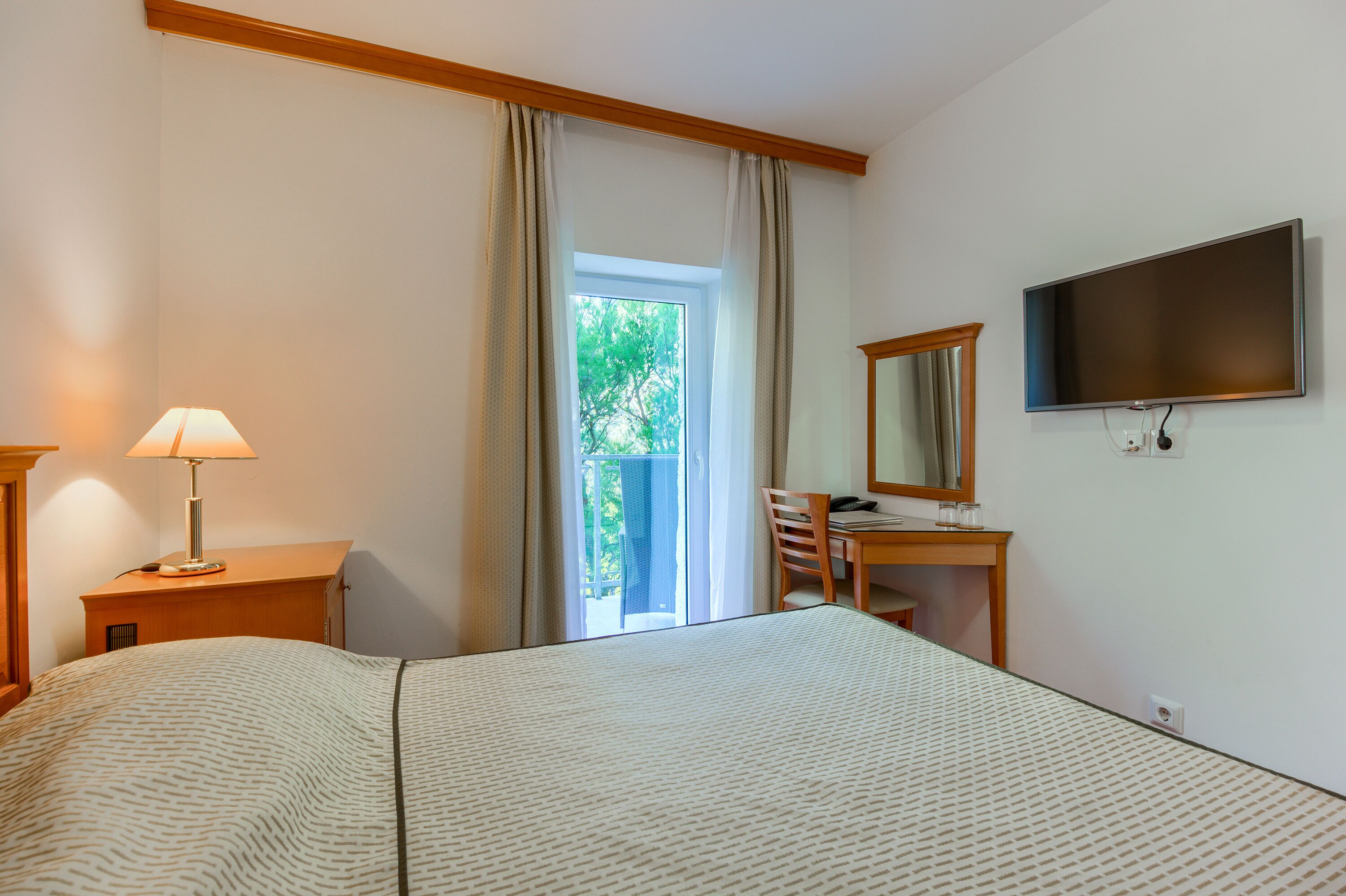 A hotel room with a bed, a desk with a chair, a television, and a window with curtains.