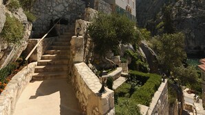 Una escalera de piedra conduce a un edificio de varios pisos con balcones, rodeado de vegetación y montañas.