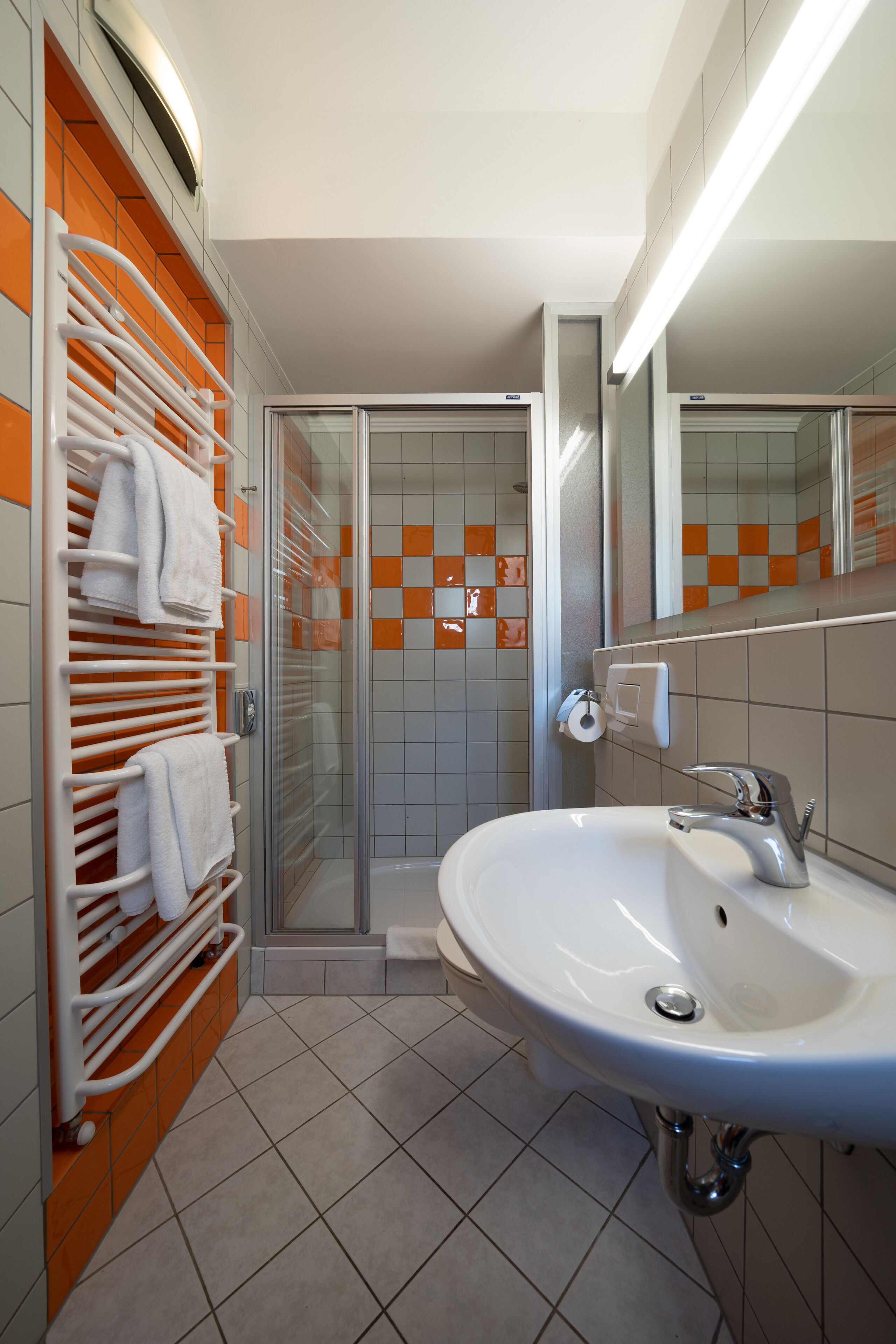 Un bagno con cabina doccia in vetro, lavandino bianco e porta asciugamani arancione.