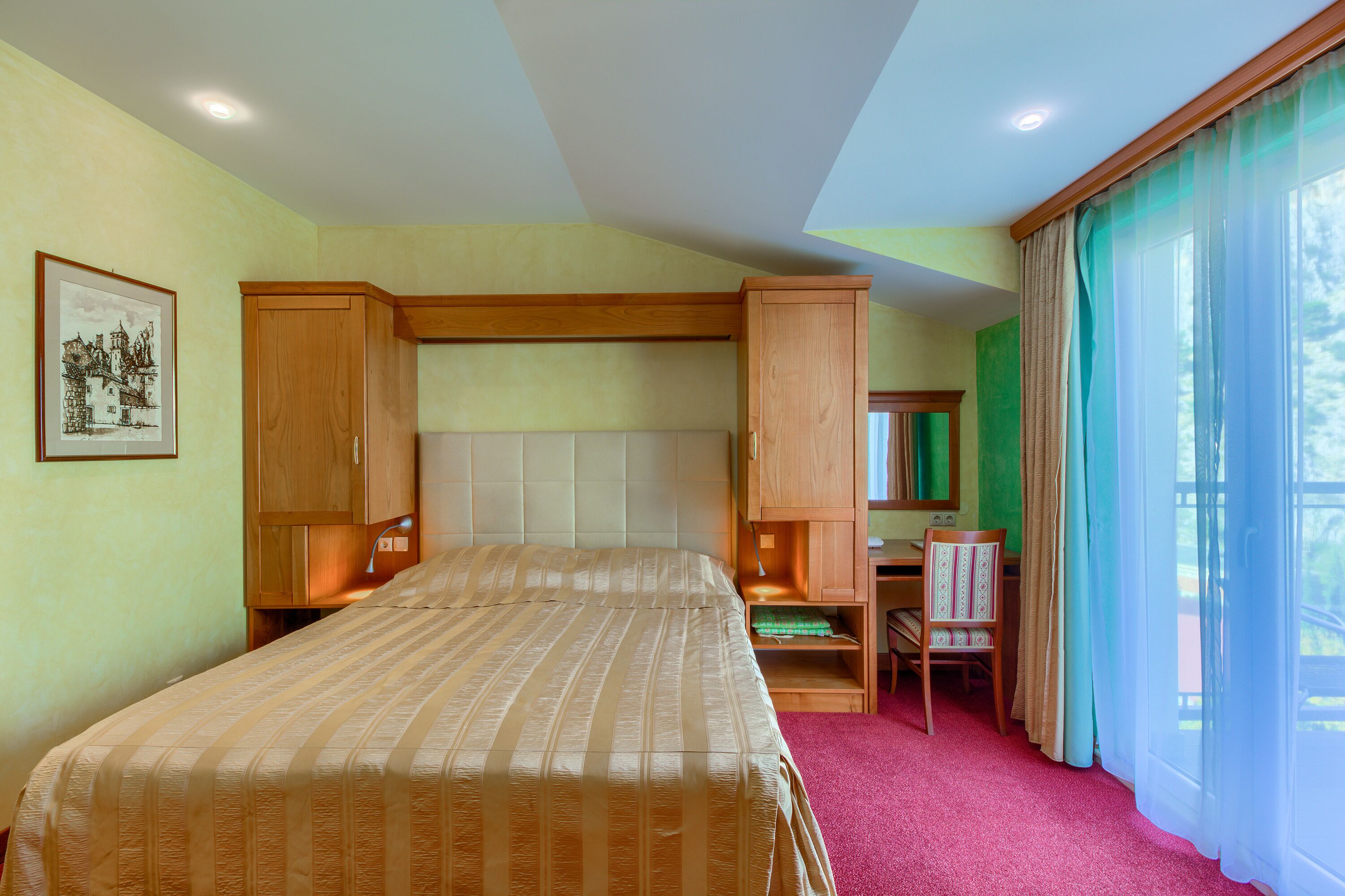 A hotel room with a large bed, a desk, a chair, and a window with curtains.
