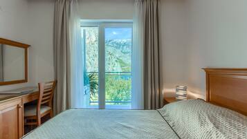A hotel room with a bed, a desk, a chair, a nightstand, and a view of a mountainous landscape through a large window.