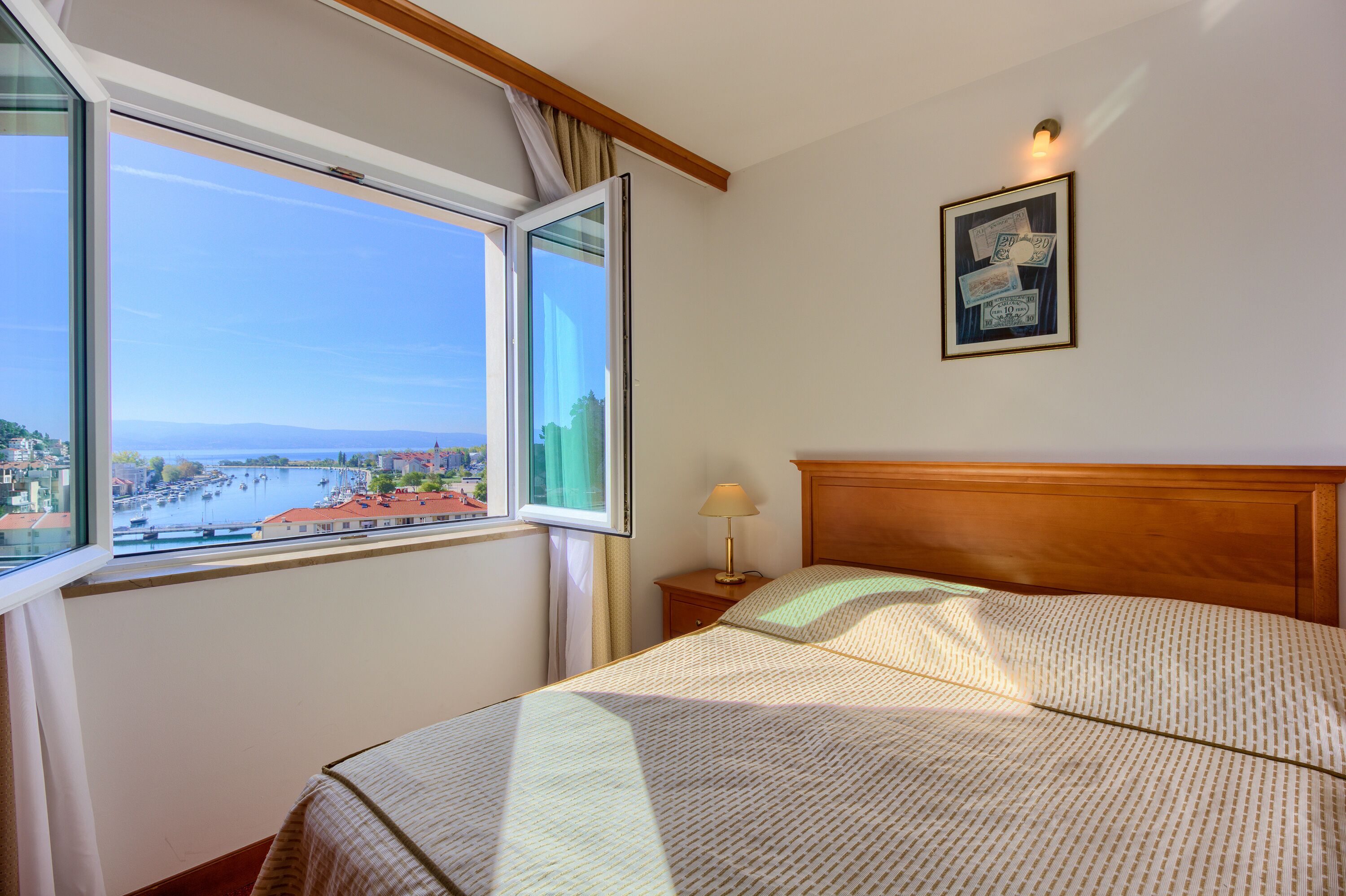 A hotel room with a large window, a bed, a nightstand, and a wall-mounted lamp.