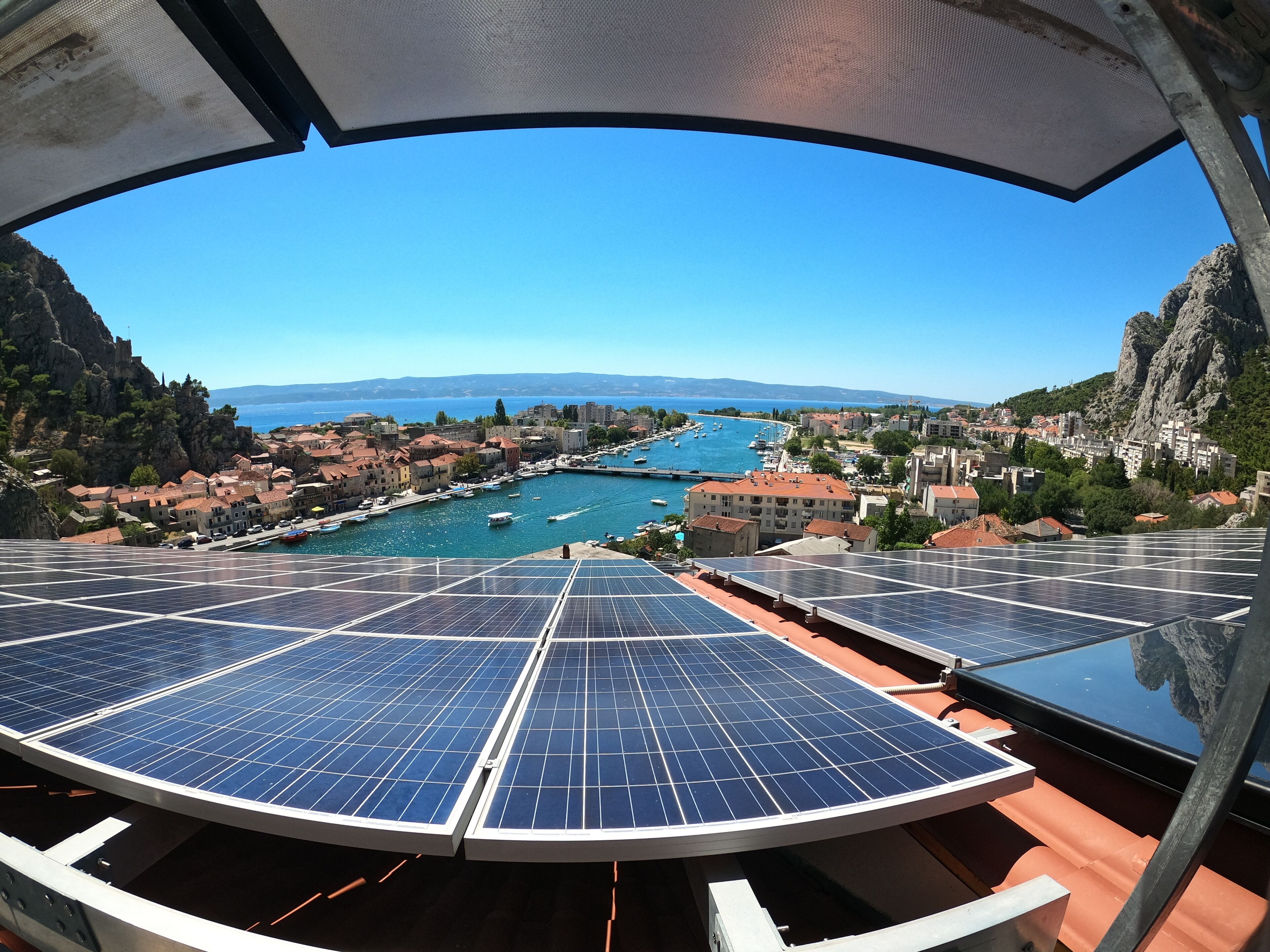A coastal town with a marina, solar panels, and mountainous terrain.