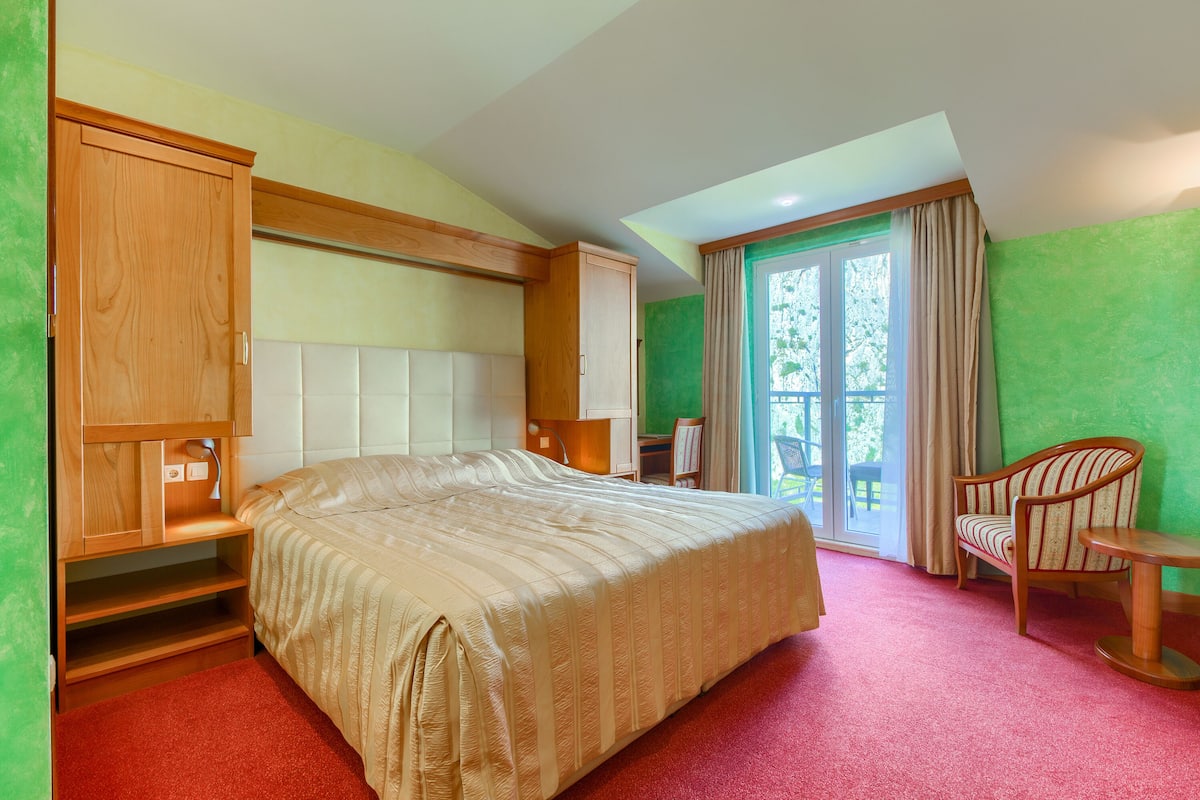 Un dormitorio con una cama grande, un armario de madera, un escritorio, una silla y vistas al exterior a través de una puerta corredera.