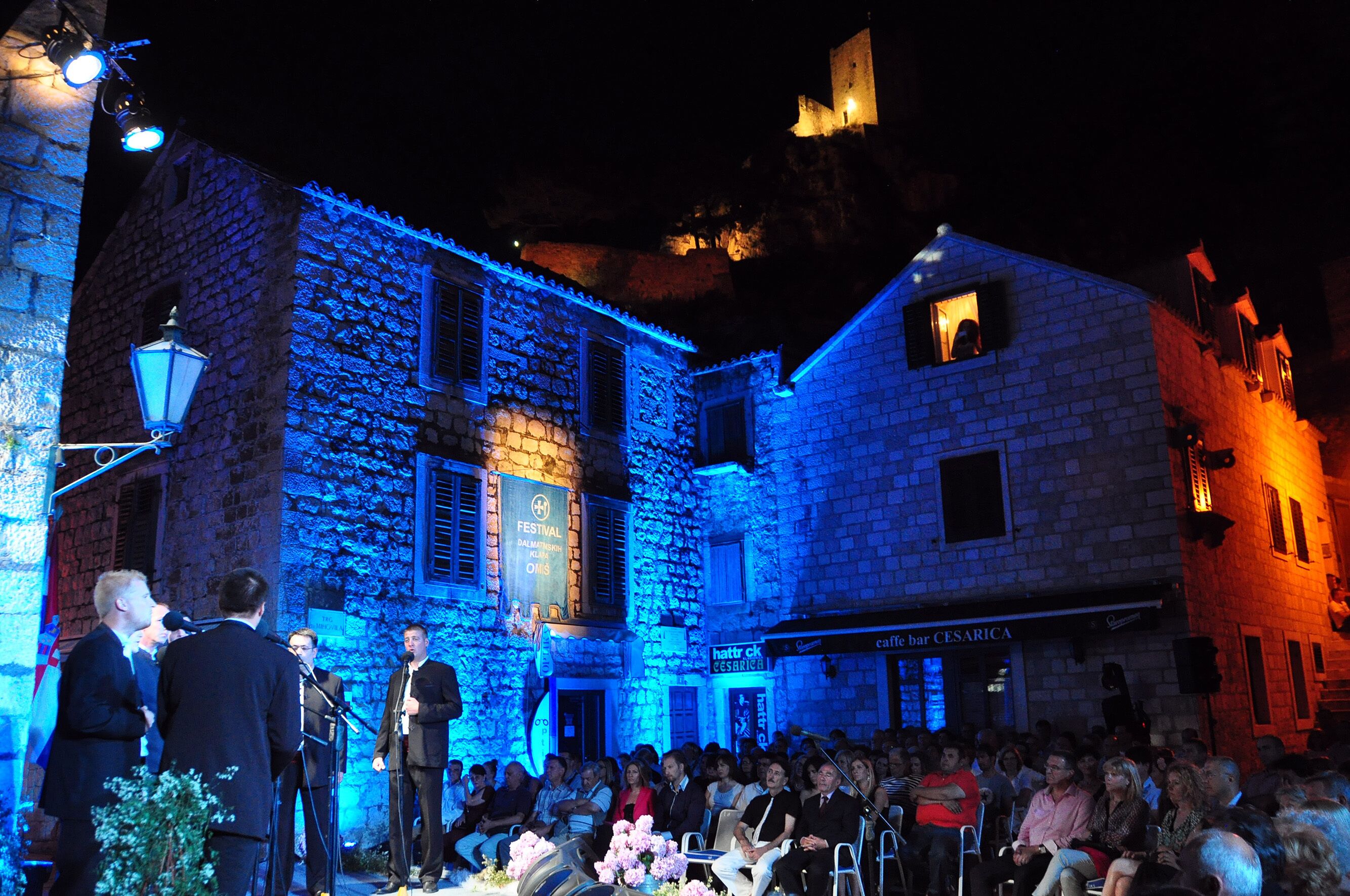A stone building with a stage and audience, featuring a sign for 'Caffare bar CESARICA'.