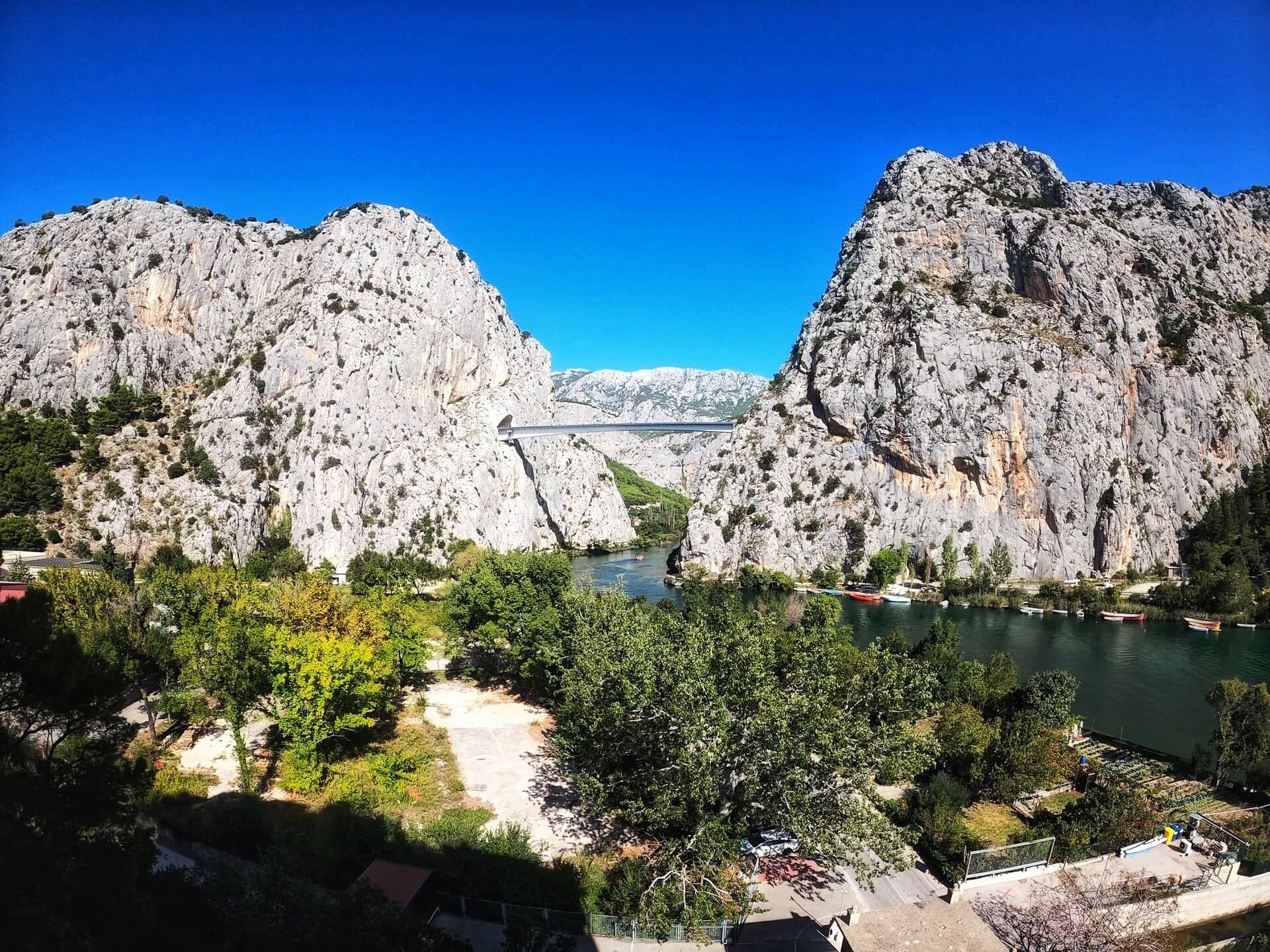A mountainous landscape with a bridge, a river, and a small settlement with buildings and greenery.