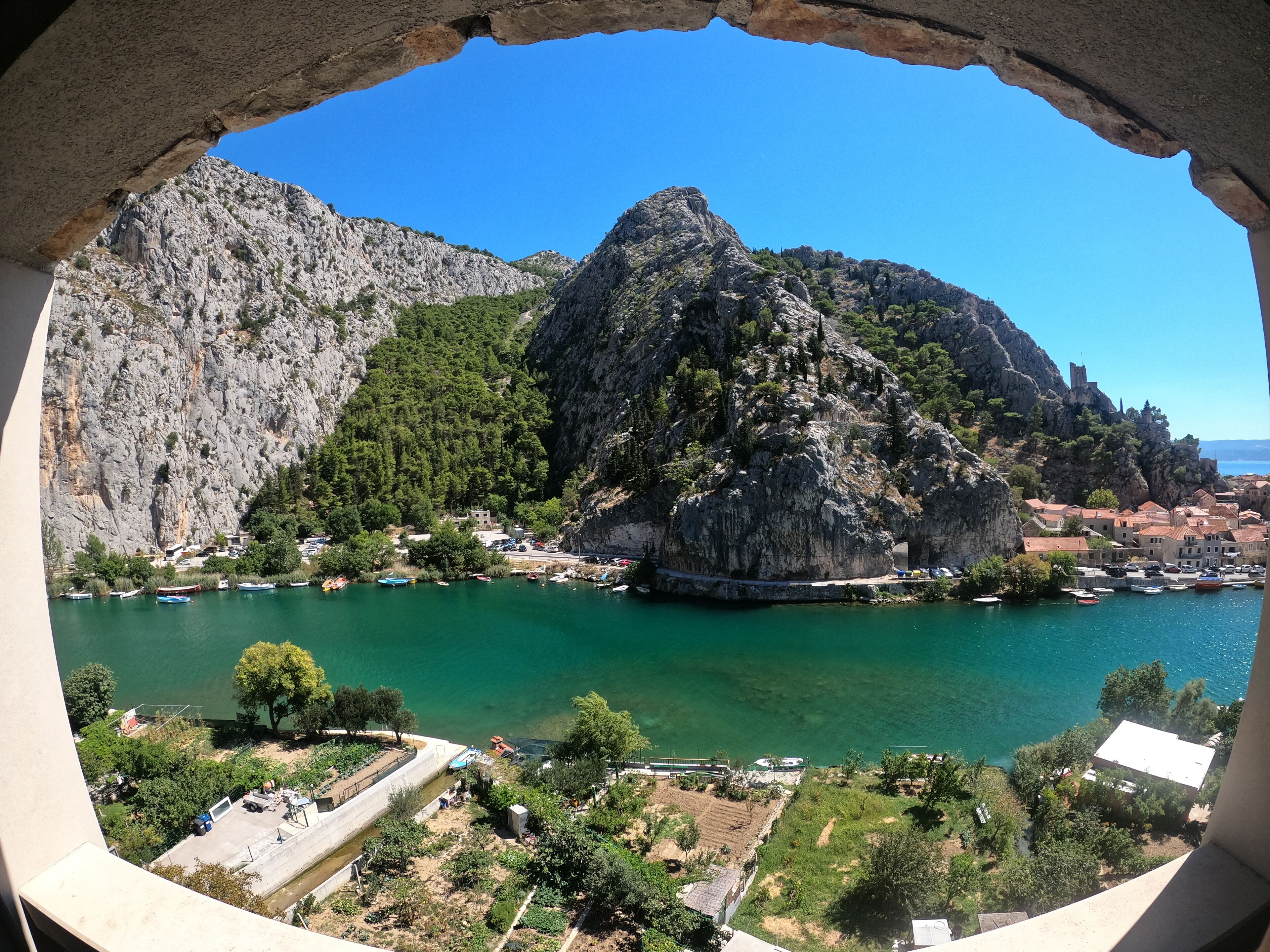 Une ville côtière caractérisée par une montagne rocheuse imposante, des eaux turquoise cristallines et un port de plaisance où sont amarrés des bateaux.