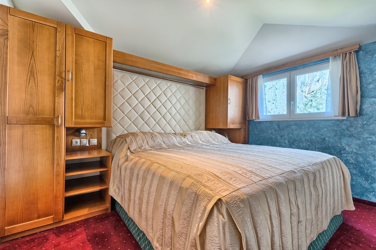 Un dormitorio con una cama grande, armario de madera, estanterías empotradas y una ventana con cortinas.