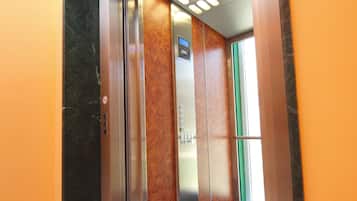 Interior d'un ascensor amb paret de marbre, porta verda i sòl gravat amb la inscripció 'Villa 1937-20'.