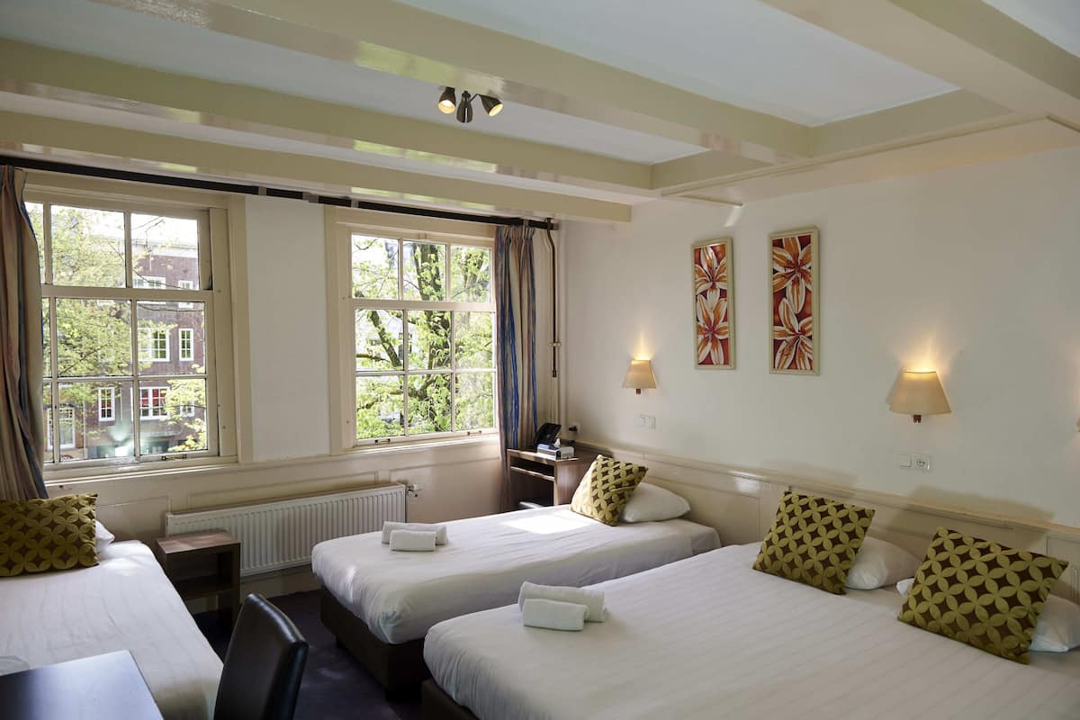 A hotel room with two beds, a desk, a chair, and a window with curtains.