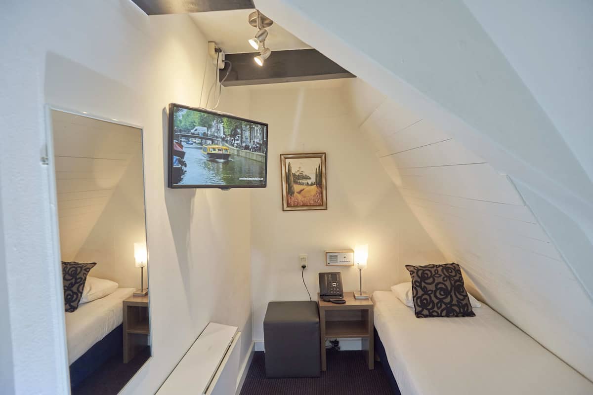 A compact hotel room with a bed, a small desk, a chair, a TV mounted on the wall, and a picture frame.
