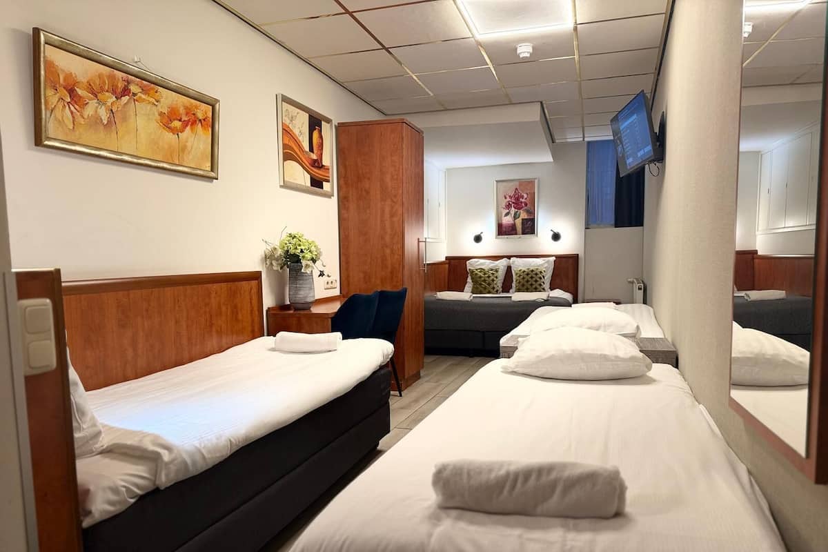 A hotel room with two beds, a wooden headboard, a small table with a vase of flowers, and artwork on the walls.