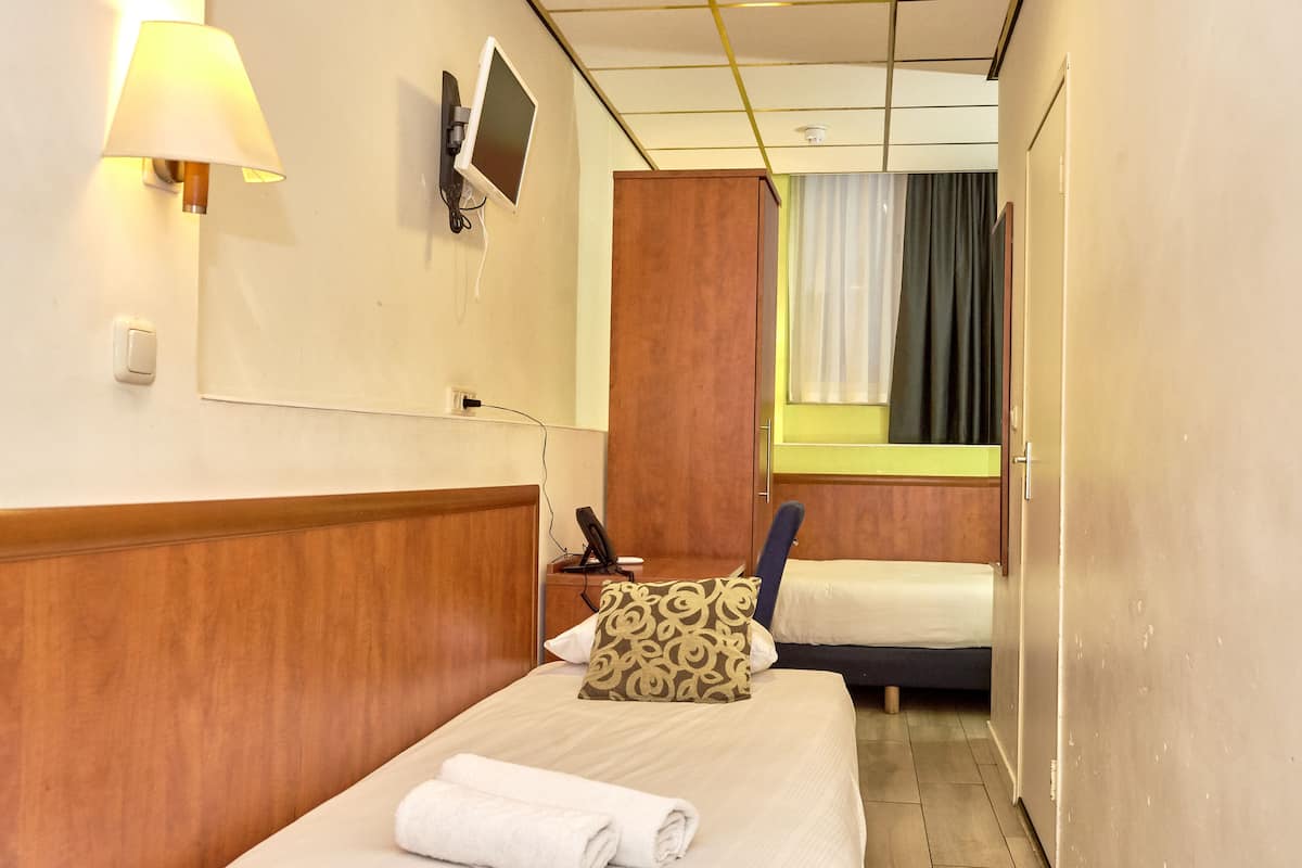 A hotel room with a bed, a bedside table with a lamp, a phone, and a window with curtains.