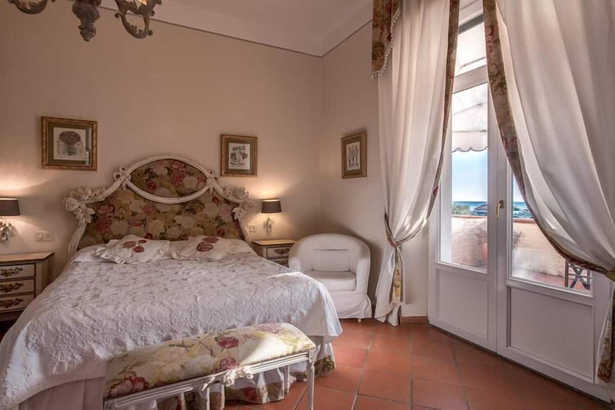 A bedroom with a bed, a chair, a nightstand, and a window with curtains.