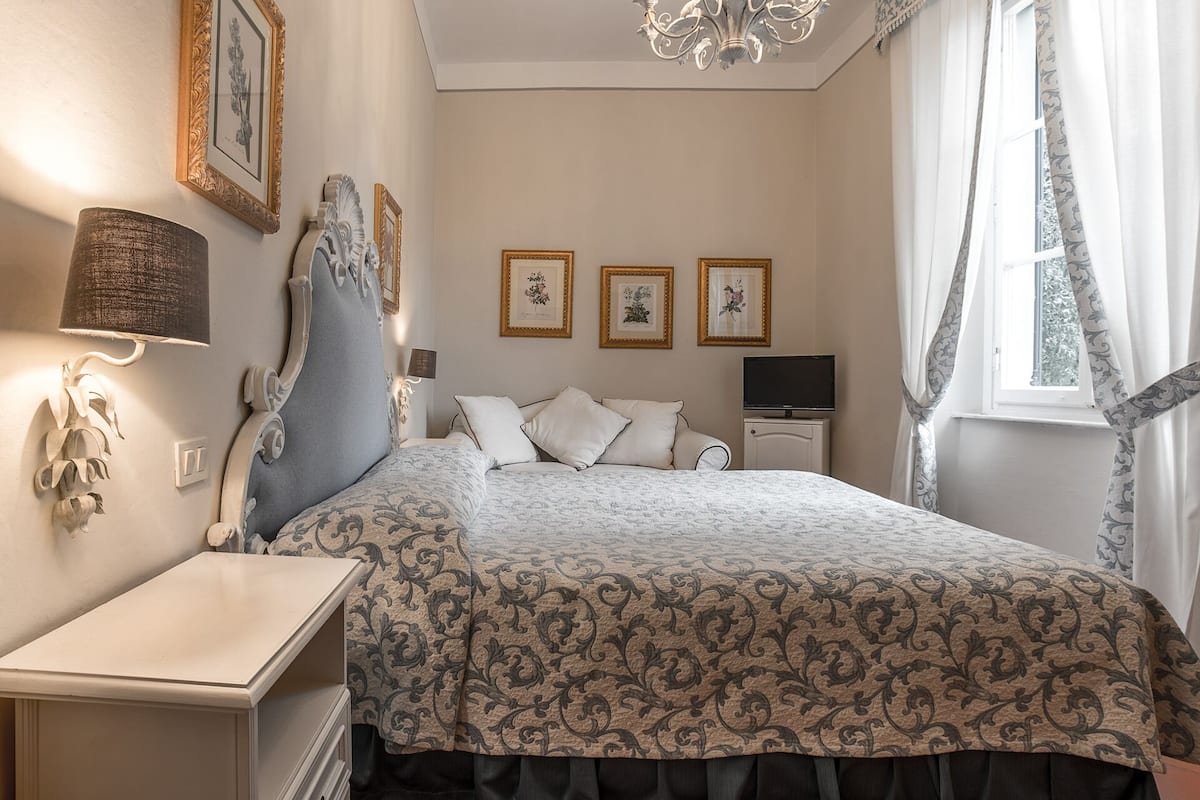 A bedroom with a bed, a bedside table, a lamp, a TV, and framed pictures on the wall.
