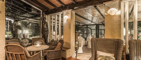 A covered patio area with wicker furniture, a statue, and a view of the garden.