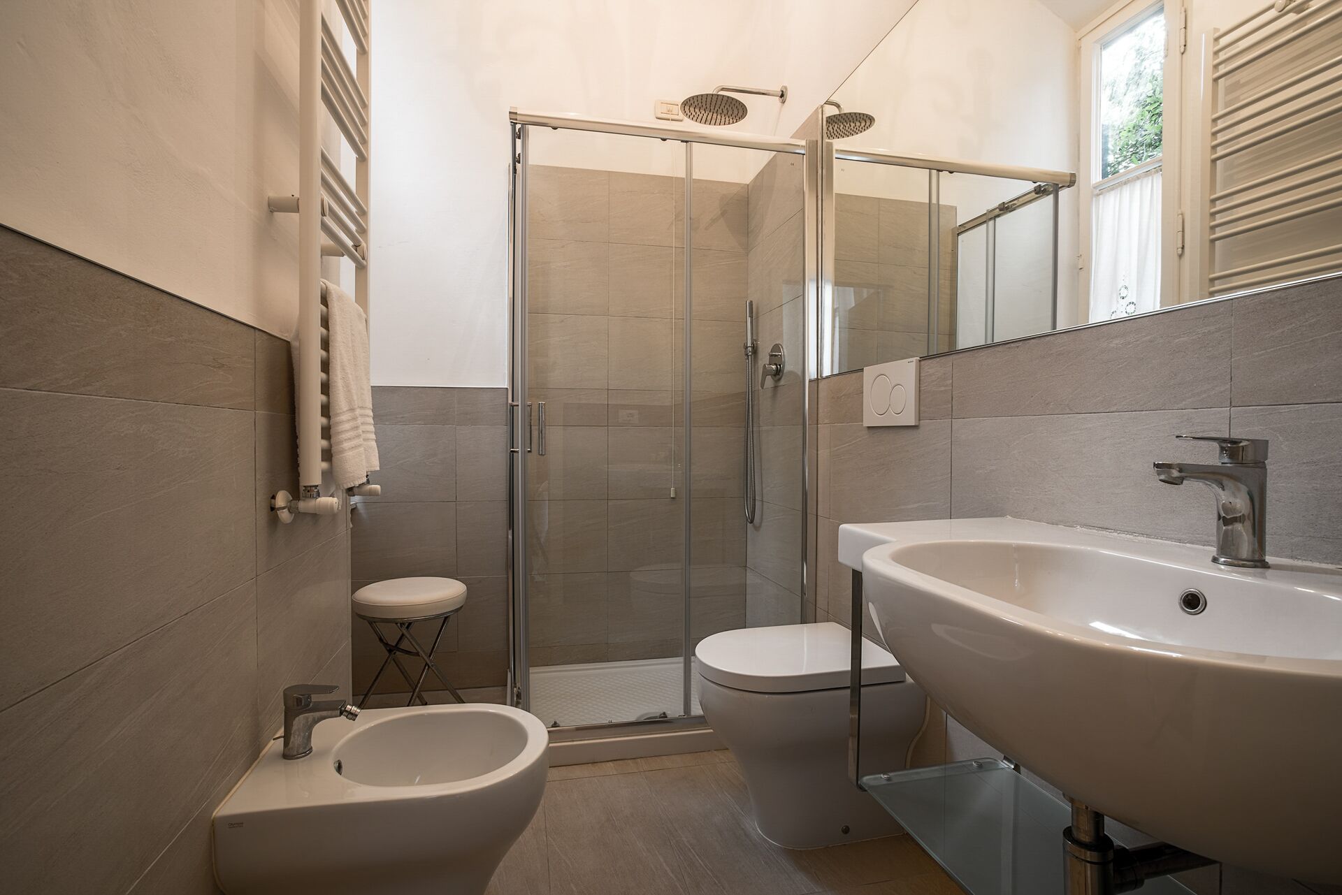 A modern bathroom with a glass-enclosed shower, a bidet, and a large sink.