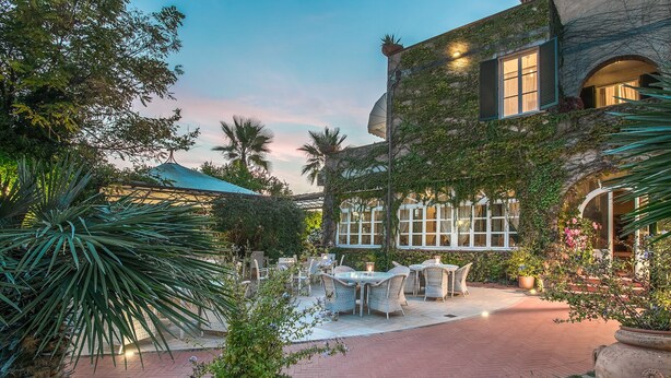 Un patio con mobiliario exterior, una zona cubierta y un edificio de piedra con hiedra.