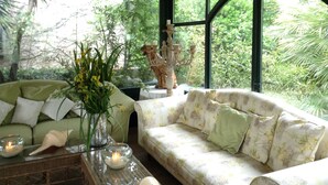 Una habitación acogedora con un sofá verde y un sofá con estampado floral, una mesita de centro de cristal con velas y una estatua decorativa.