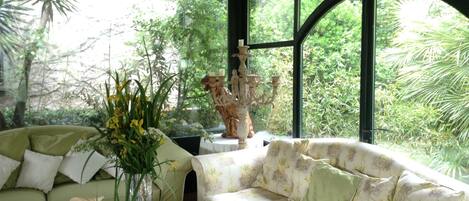 A cozy room with a green sofa and a floral-patterned couch, a glass coffee table with candles, and a decorative statue.