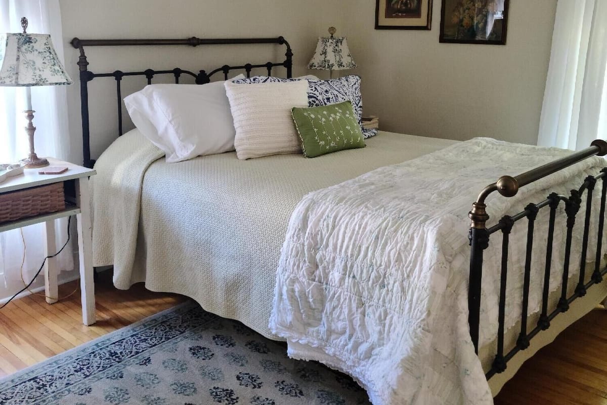 A bedroom with a bed, a nightstand, a lamp, a ceiling fan, and framed pictures on the wall.