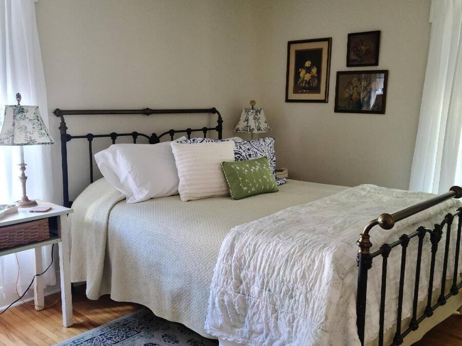 A bedroom with a bed, a nightstand, a lamp, a ceiling fan, and framed pictures on the wall.