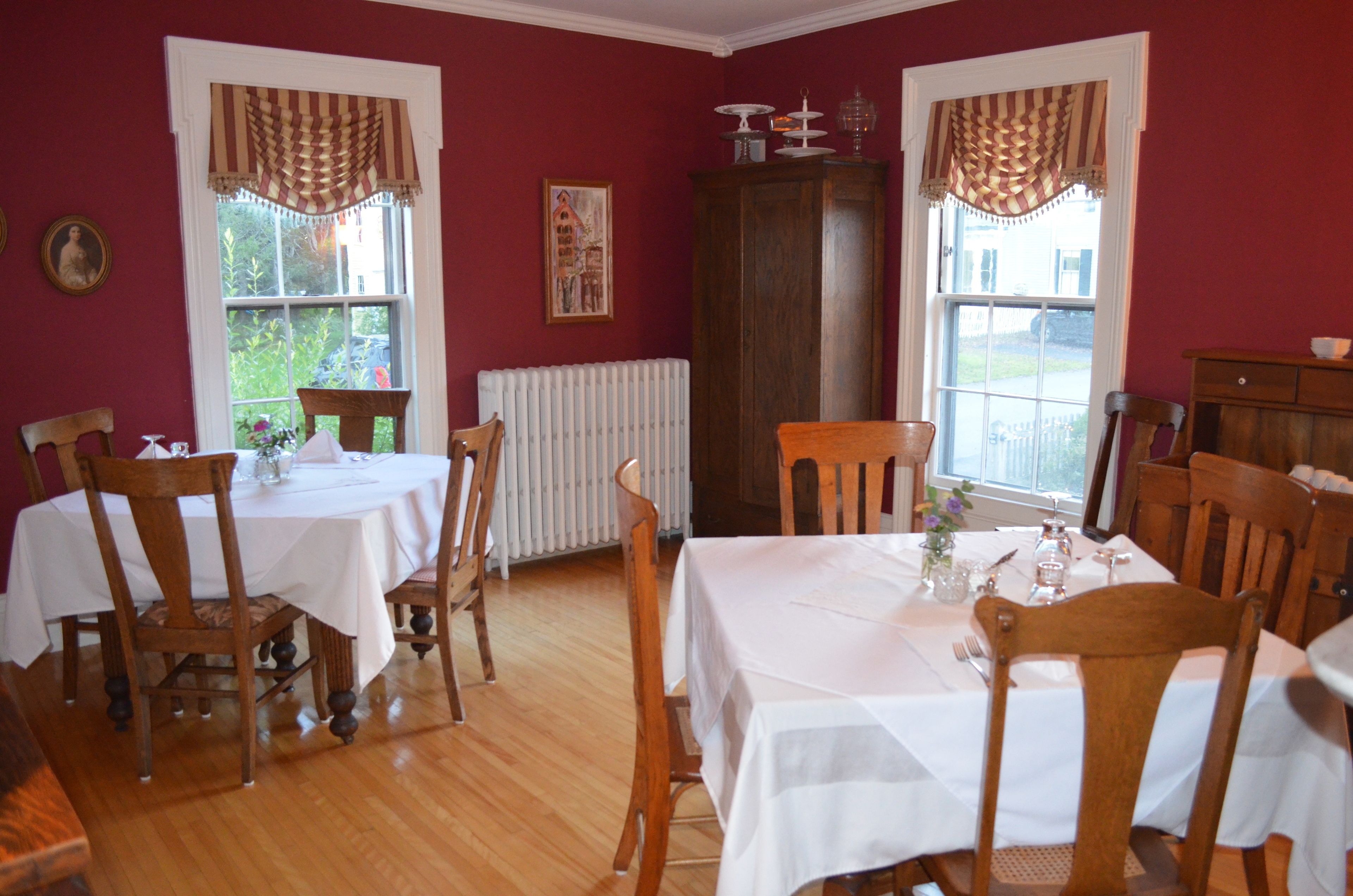 A dining room with two tables set for six, wooden chairs, a radiator, and a large cabinet.