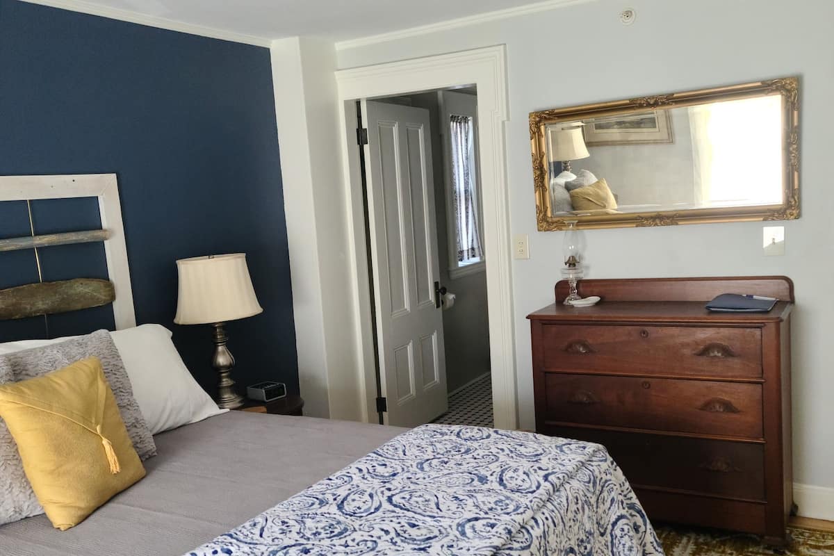 A bedroom with a bed, a dresser, a mirror, and a door leading to another room.