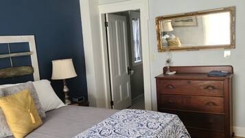 A bedroom with a bed, a dresser, a mirror, and a door leading to another room.