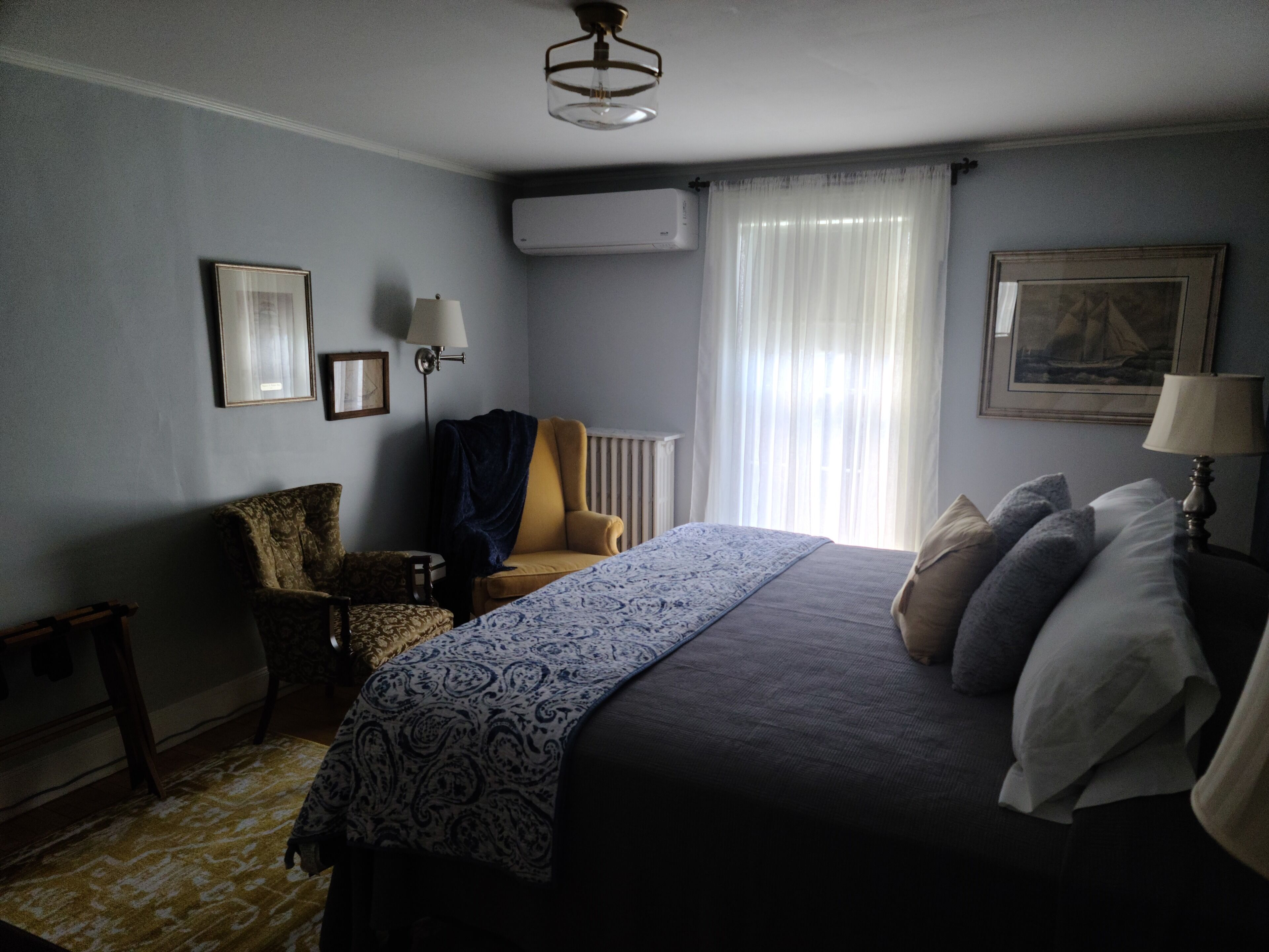A bedroom with a bed, a chair, a lamp, a radiator, and a window with curtains.