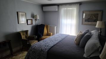 A bedroom with a bed, a chair, a lamp, a radiator, and a window with curtains.