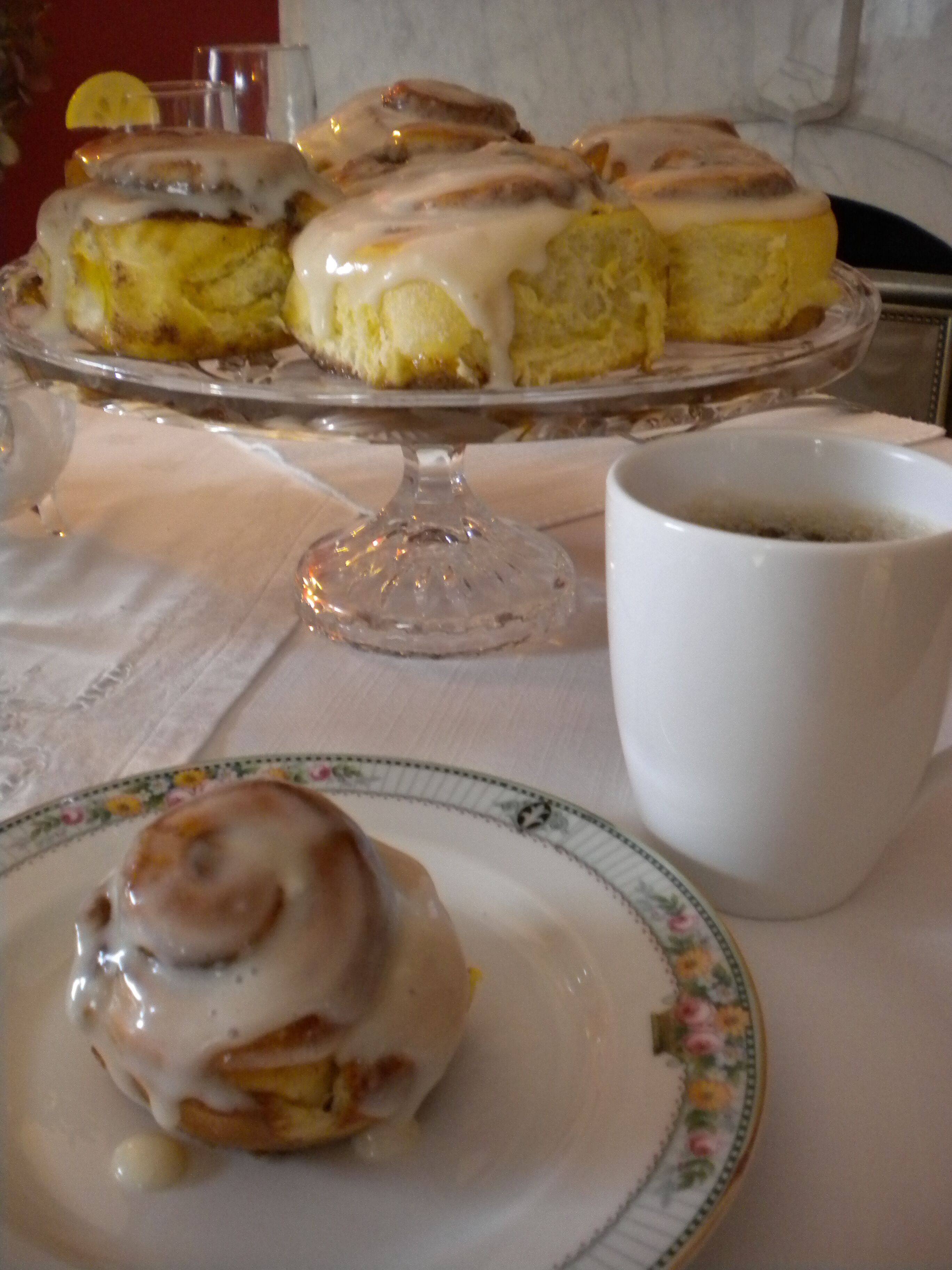 A breakfast setting with a plate of cinnamon rolls, a cup of coffee, and a glass of water on a table.